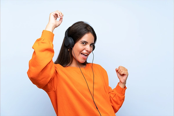 Woman in orange sweatshirt dancing with headphones on