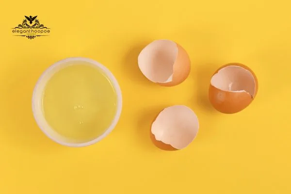 Bowl of whipped egg whites with three eggshell halves on a yellow surface
