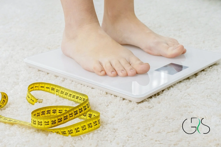 Bare feet on digital scale next to tape on carpet 