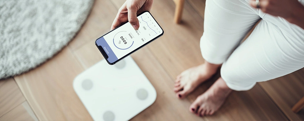 Woman checking her BMI data on a mobile app connected to a smart digital scale