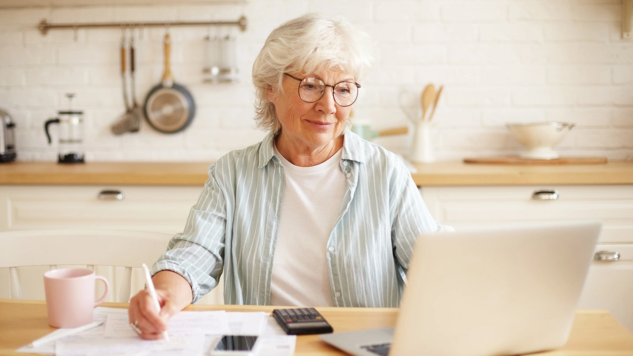 Senior woman calculating her BMI using a laptop in a kitchen setting