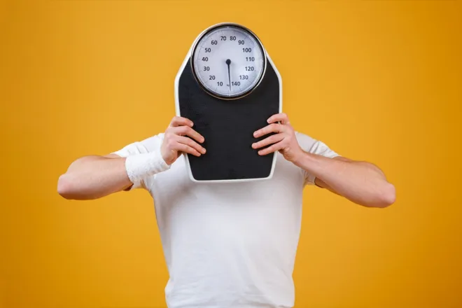 Man holding a weight scale in front of his face on yellow background