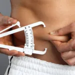 Person using skinfold calipers to measure abdominal body-fat fold for BMI and body-fat calculator article.