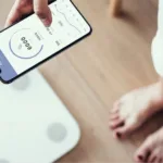 A person checking BMI and weight data on a smartphone app connected to a smart scale.