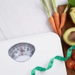 Analog bathroom scale surrounded by vegetables and measuring tape showing what you need to calculate BMI
