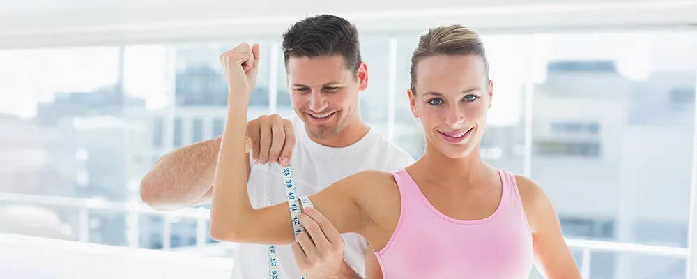 Close-up of a fitness trainer measuring a person’s upper arm circumference with a yellow tape to assess muscle mass