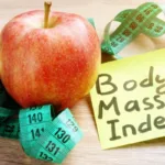 Green apple next to a pink heart-shaped card and measuring tape, symbolizing holistic health and the Body Index concept.