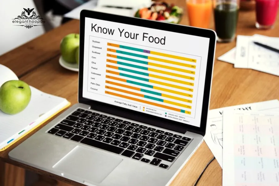 Laptop screen showing a colorful chart comparing fatty acid values of different oils, surrounded by apples, notebooks, and drinks on a table.