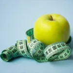 Green apple encircled by measuring tape on blue background