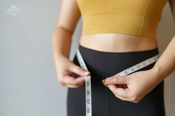 A person measuring their waist with a tape measure, highlighting the importance of tracking body measurements for calculating muscle mass percentage
